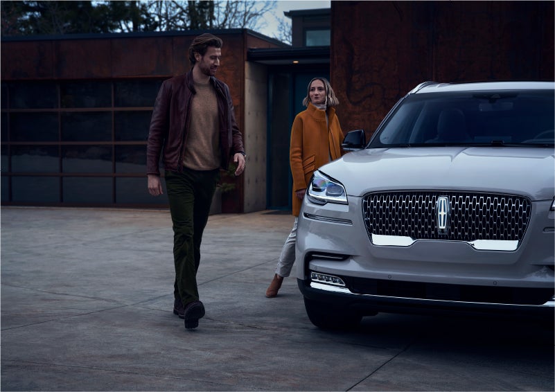 A man and a woman approaching a 2023 Lincoln Aviator® SUV, which illuminates certain lights when they are close | Mike Reichenbach Lincoln in Florence SC