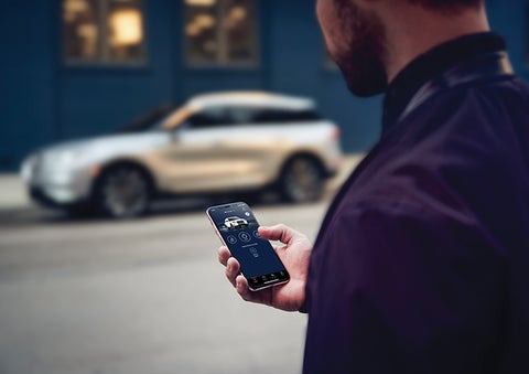 A person is shown interacting with a smartphone to connect to a Lincoln vehicle across the street. | Mike Reichenbach Lincoln in Florence SC